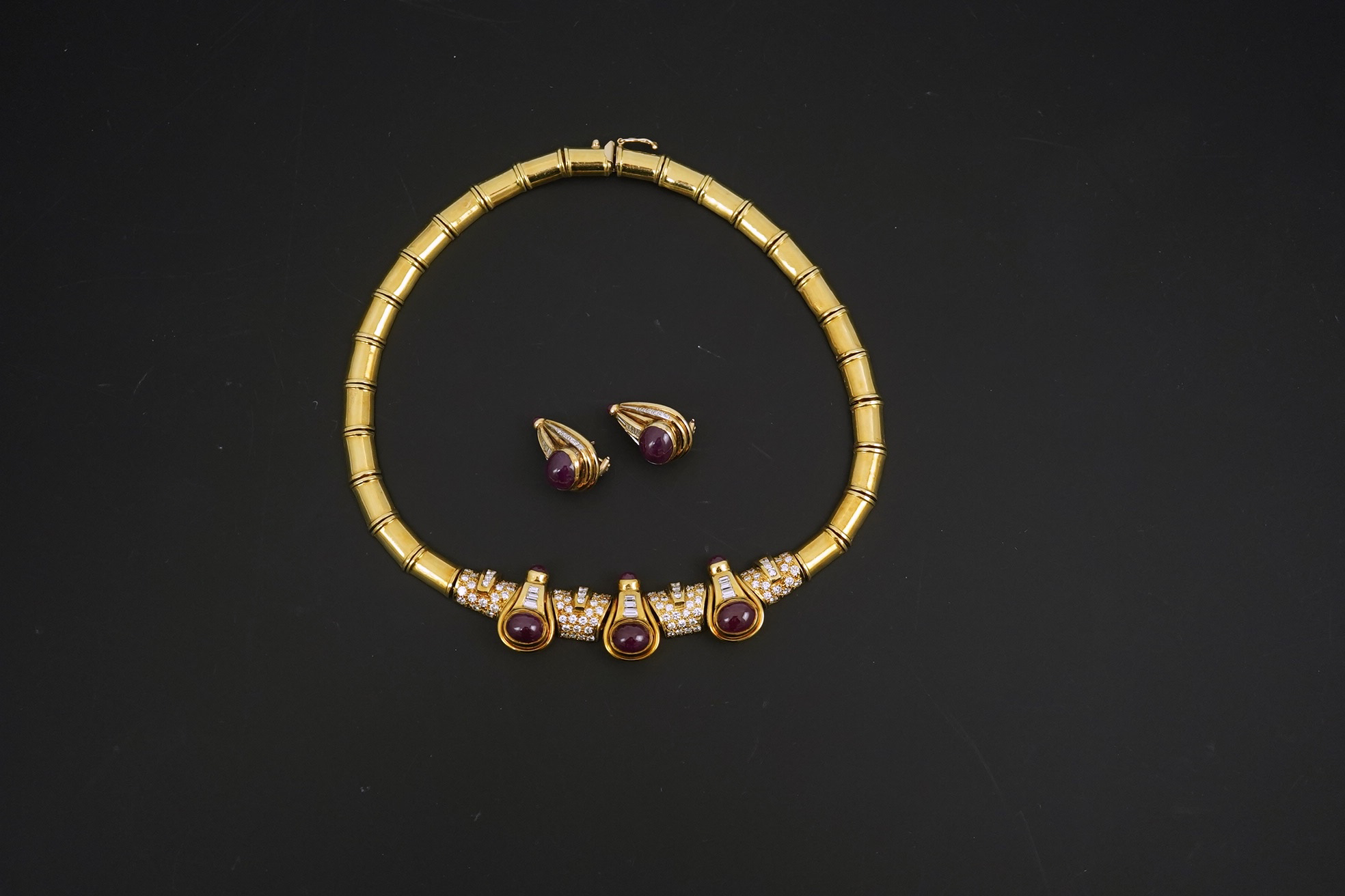 A modern 18k gold, cabochon ruby, round and baguette cut diamond cluster set torque necklace and a pair of matching earrings